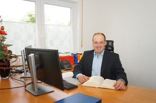 Johannes Burggraf mit aufgeschlagenem Buch an seinem Schreibtisch sitzend